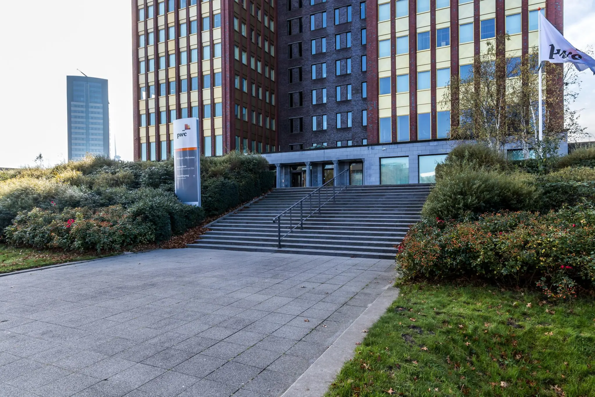 Ingang van het PwC-kantoor aan de Fascinatio Boulevard met trappen, vlag en omliggende beplanting.